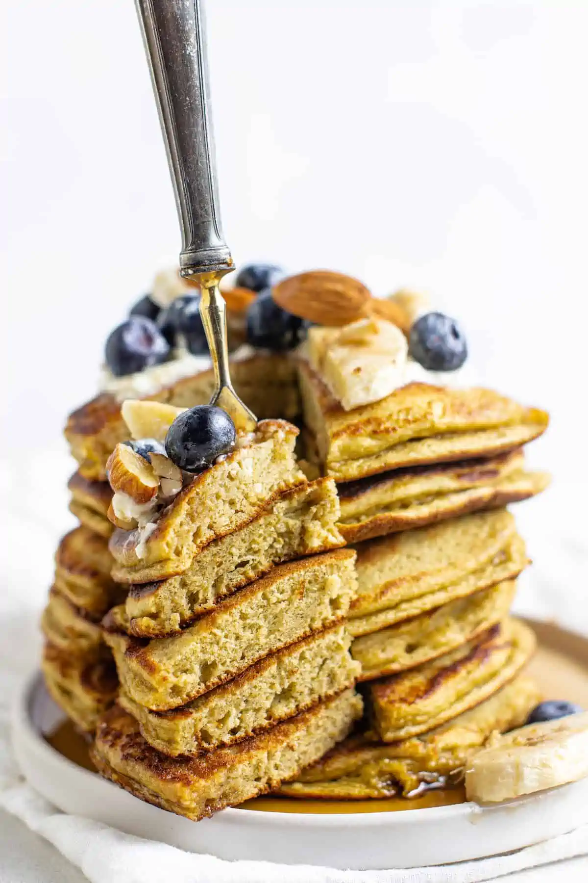 These protein pancakes are fluffy and flavorful, made with 6 ingredients in the blender. Gluten-free, dairy-free, and meal prep-friendly! A fork stuck into a stack of protein pancakes topped with fruit and nuts.