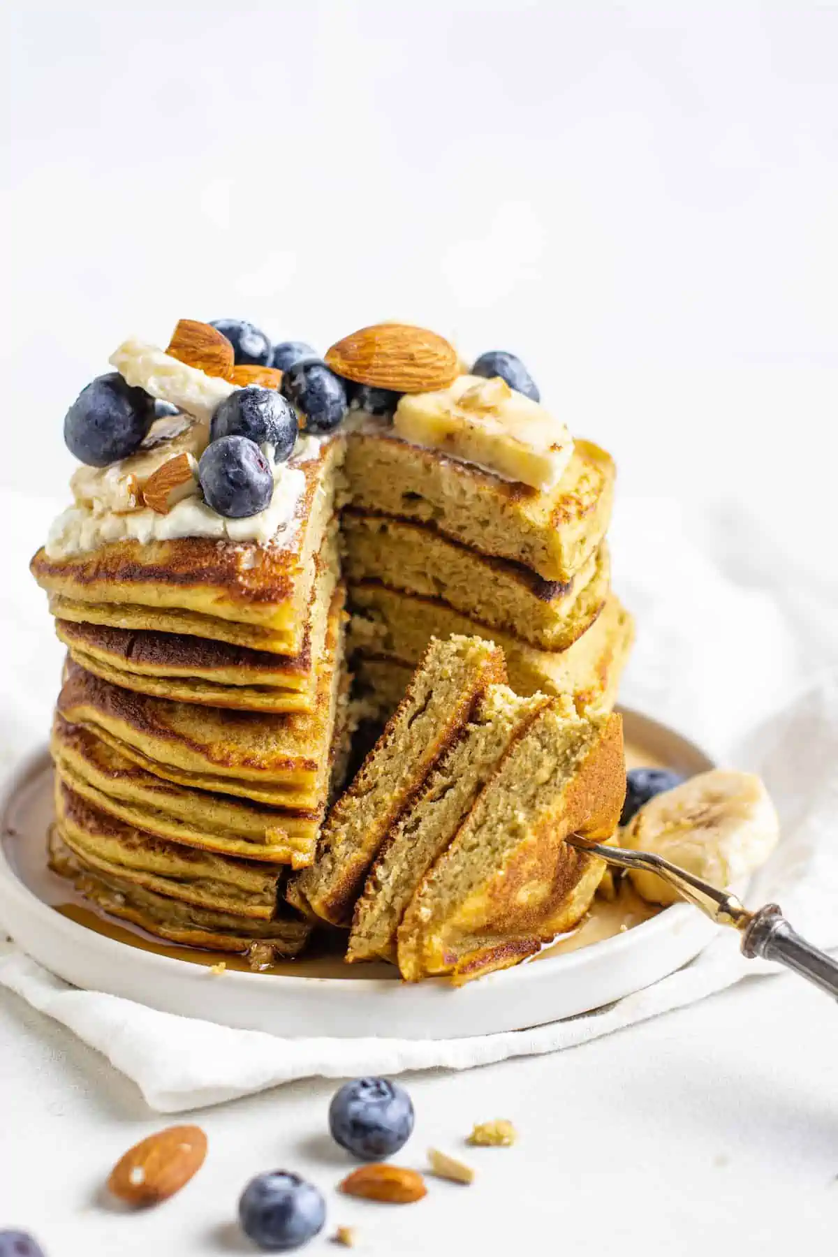 These protein pancakes are fluffy and flavorful, made with 6 ingredients in the blender. Gluten-free, dairy-free, and meal prep-friendly! A fork stuck into a portion cut from a stack of protein pancakes topped with fruit and nuts.