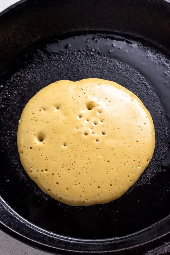 These protein pancakes are fluffy and flavorful, made with 6 ingredients in the blender. Gluten-free, dairy-free, and meal prep-friendly! A circle of bubbling pancake batter in a hot skillet.