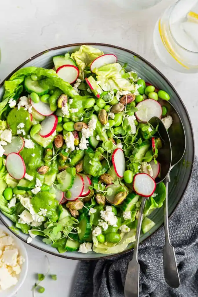 Top view of a green goddess salad in a large bowl with a serving spoon.
