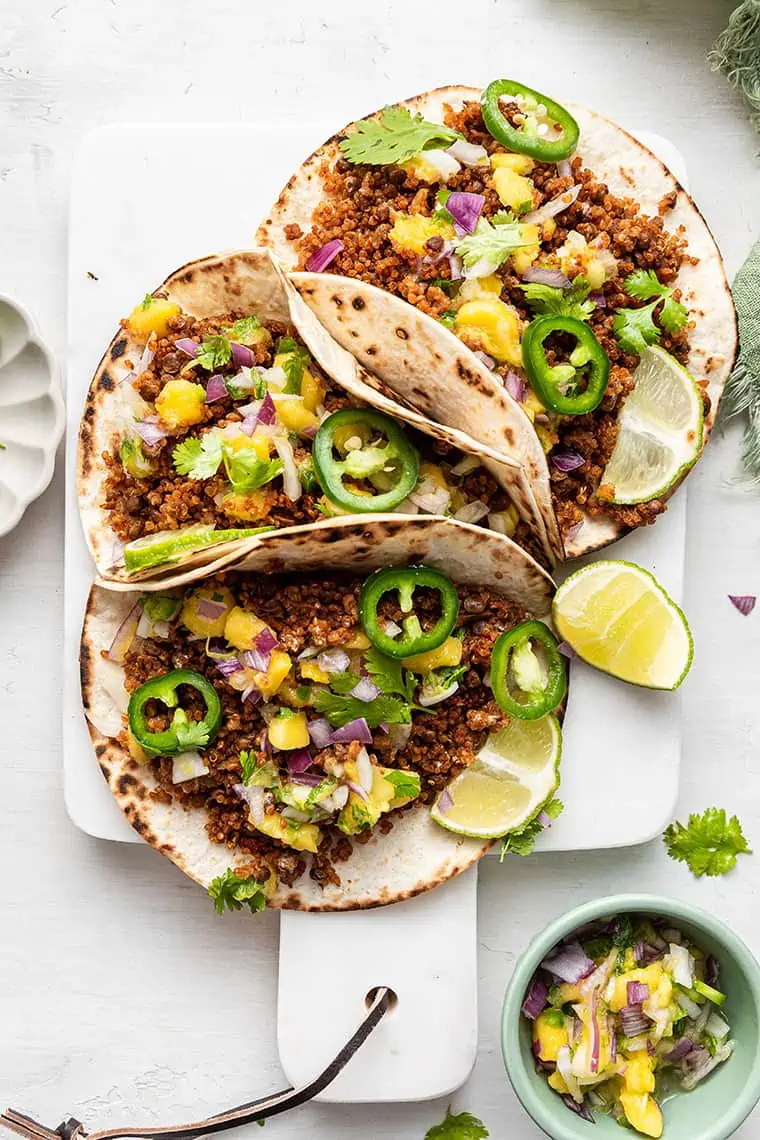 This easy vegan taco meat is made with lentils and quinoa. Unbelievably delicious, super healthy, and ideal for meal prep! Three vegan tacos on white board with garnishes and lime wedges