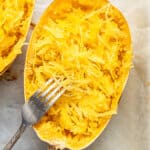 Close up of a half of a cooked spaghetti squash that's been shredded, with a fork leaning against it