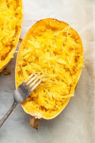 Close up of a half of a cooked spaghetti squash that's been shredded, with a fork leaning against it