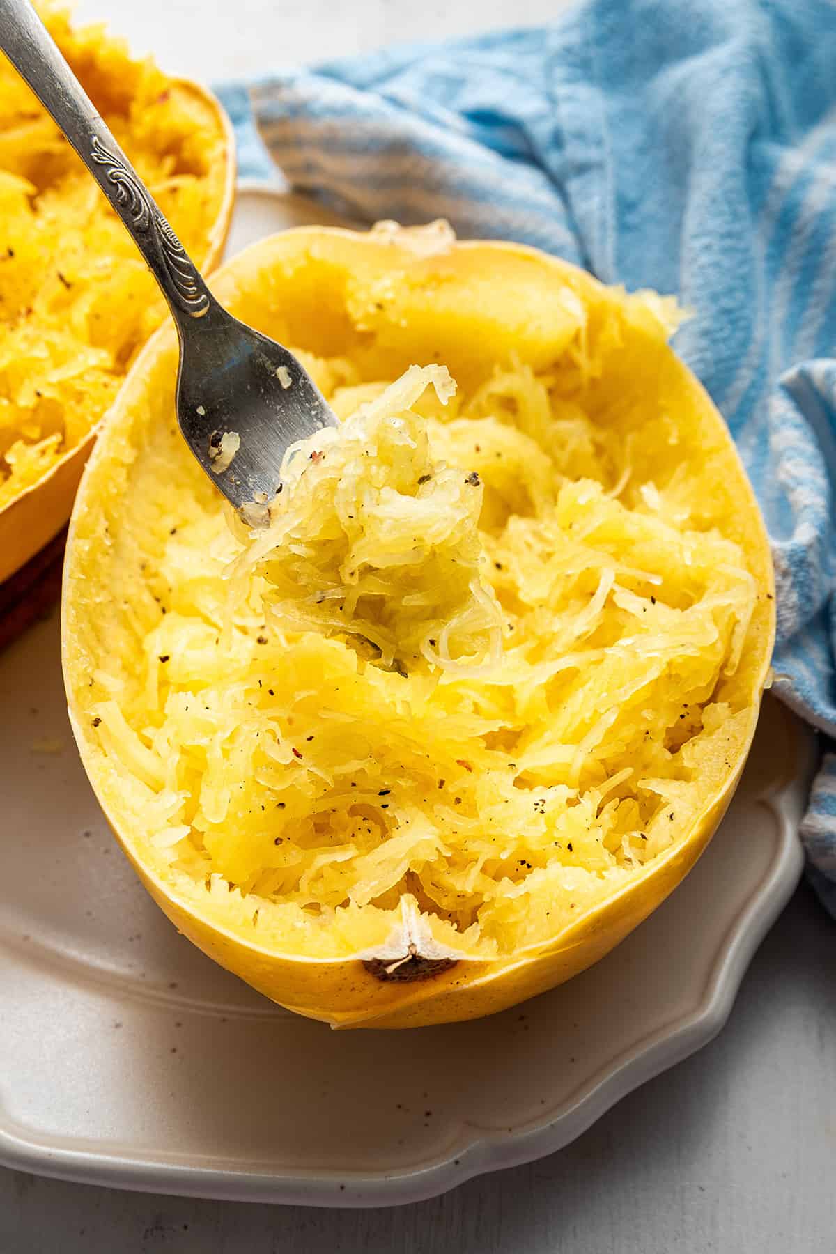 Close up of a half of a cooked spaghetti squash that has been shredded, with a fork sticking out of it
