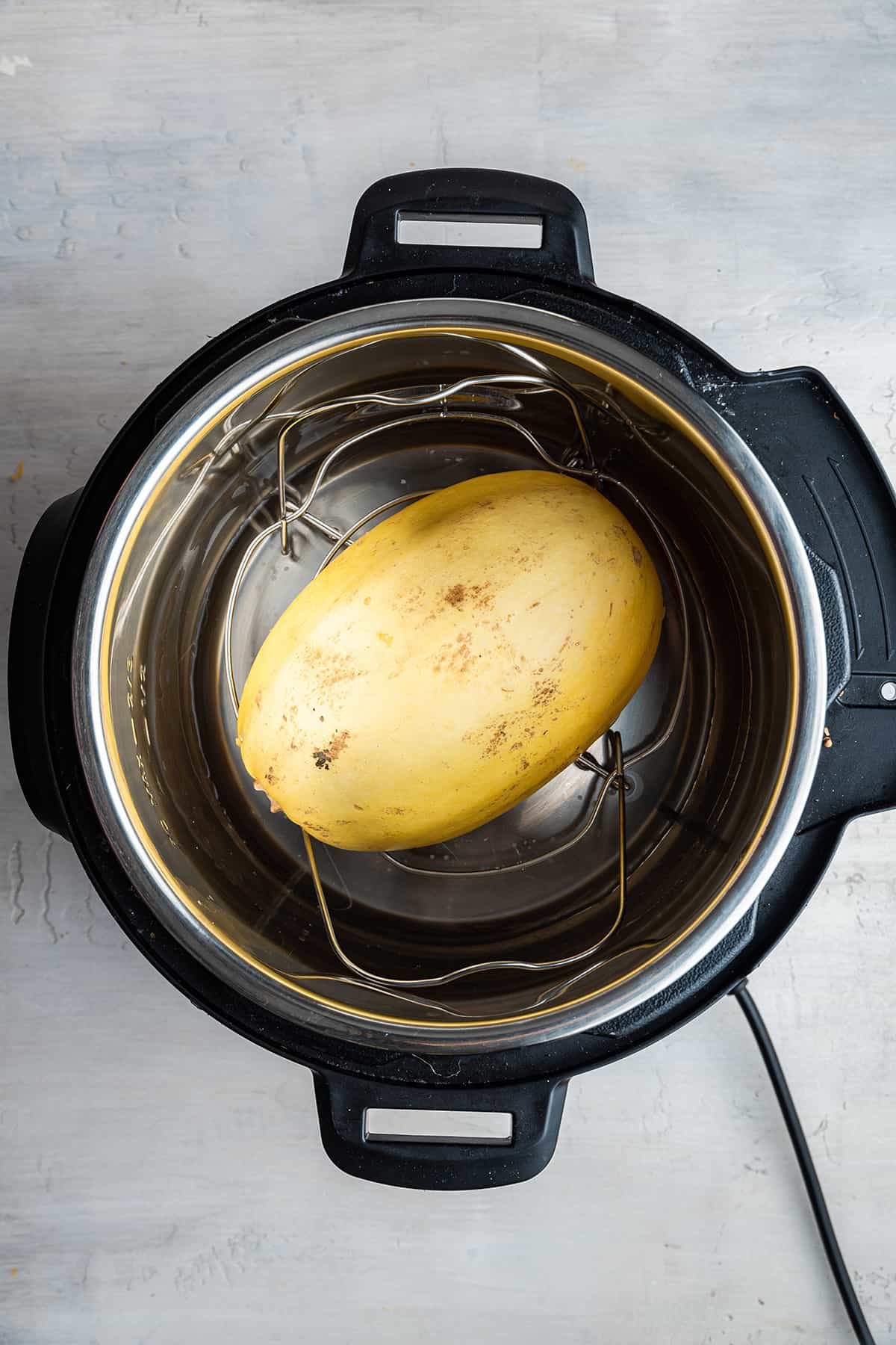 Half of an uncooked spaghetti squash face down in an instant pot