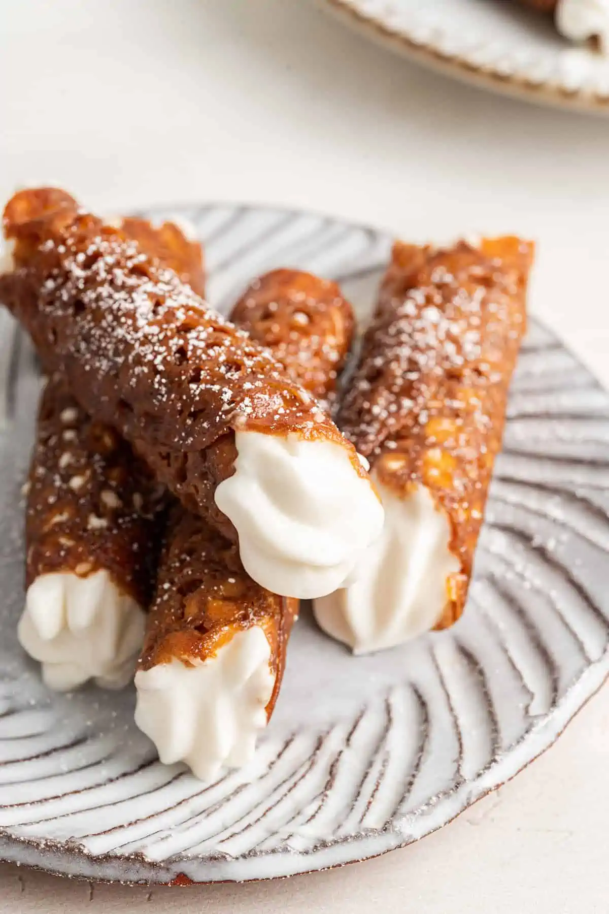 Three finished brandy snaps in a line on a plate, with a fourth lying on tnop of them