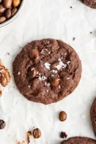 Overhead view of a single espresso cookie, topped with flaky salt, surrounded by espresso beans