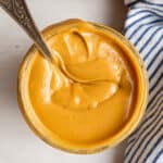 Overhead view of a jar of honey roasted peanut butter with a spoon sticking out, with a kitchen towel next to it