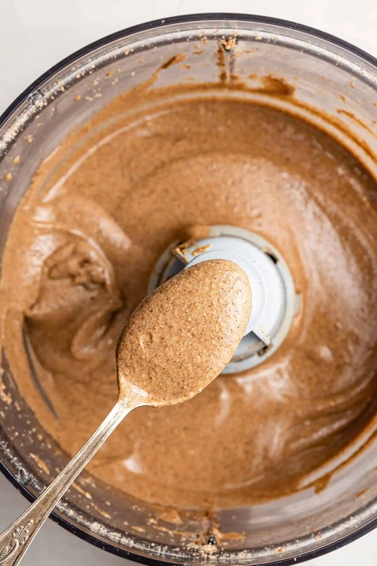 A spoon filled with pumpkin spice almond butter, above an open food processor filled with pumpkin spice almond butter