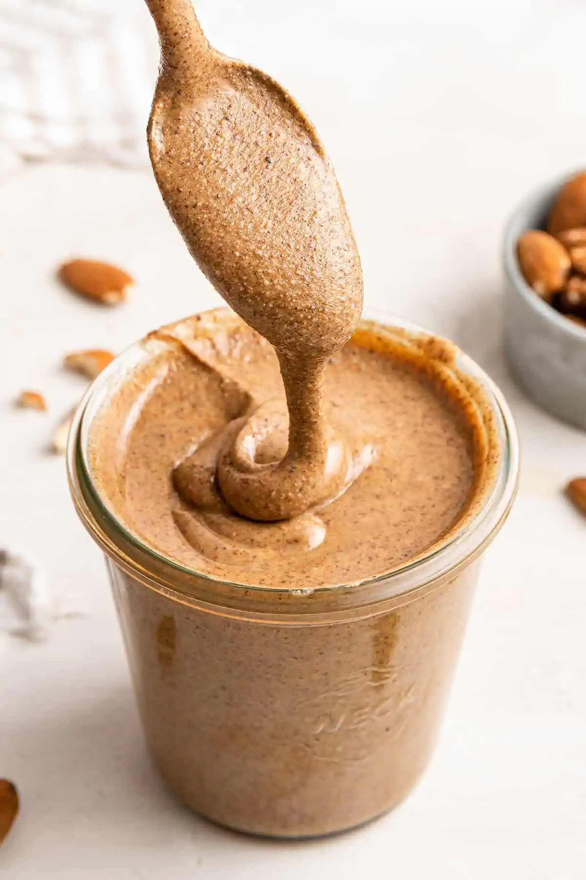 Foods that are high in magnesium are common and delicious, and can help you get all the nutrients your body needs to function. A spoonful of pumpkin spice almond butter drizzling the almond butter into a full jar of it, with a bowl of almonds in the background