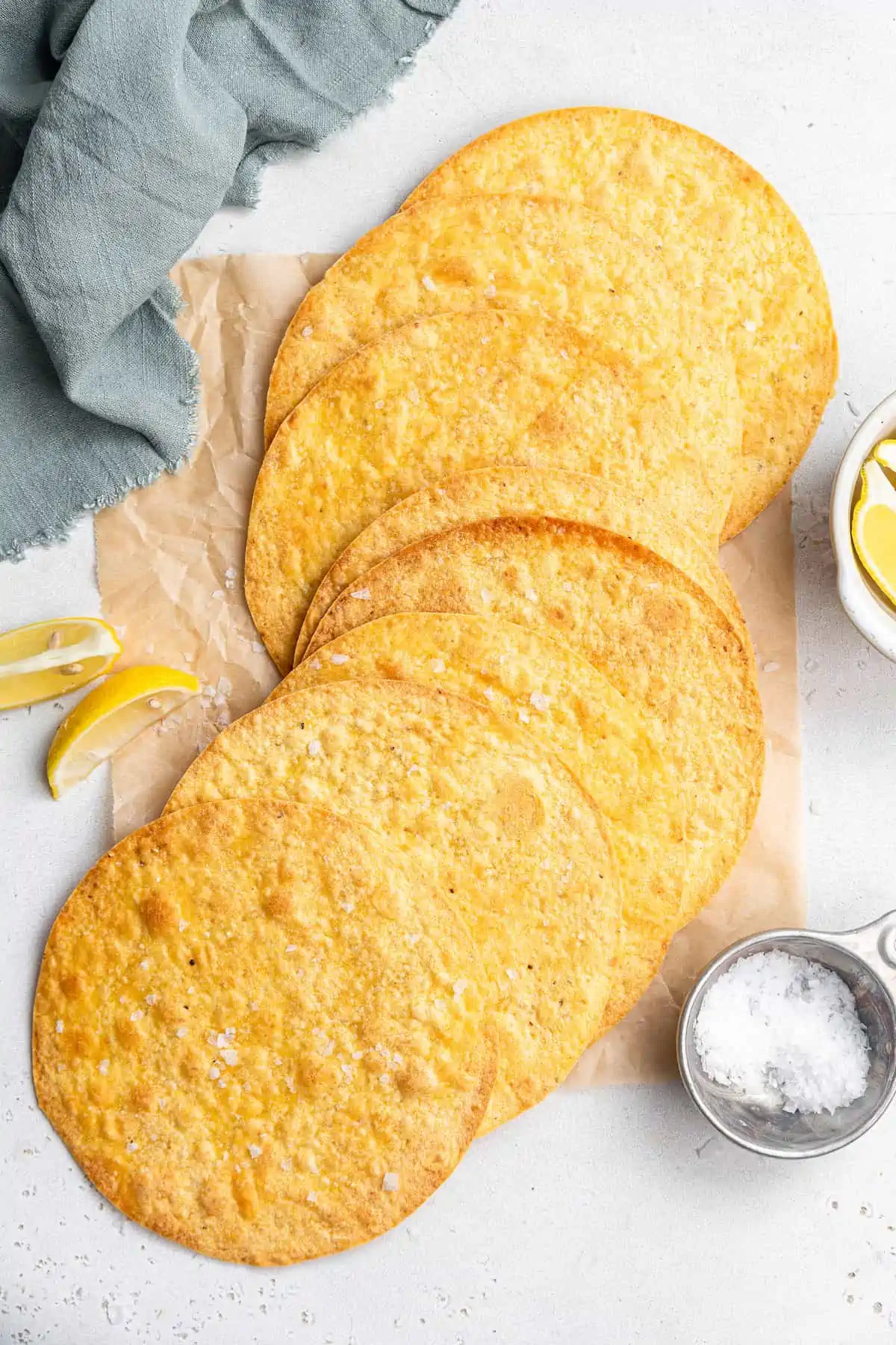 Learn to make homemade tostada shells that are golden-baked, crispy, and seasoned with flaky salt. No frying, and they're ready in 10 minutes! Overhead view of assorted tostada shells next to a small dish of flaky salt.