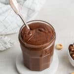 A jar of homemade nutella on a coaster, with a spoon in it.
