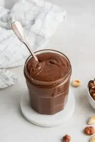 A jar of homemade nutella on a coaster, with a spoon in it.