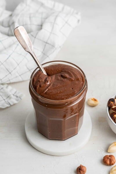 A jar of homemade nutella on a coaster, with a spoon in it