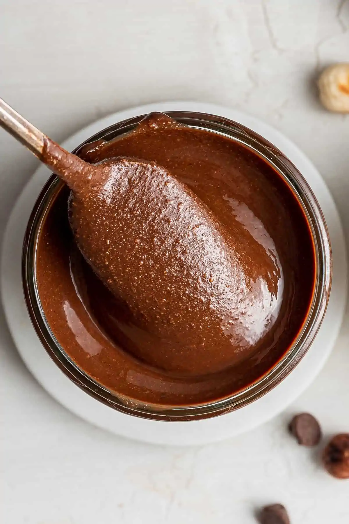 Close up of a spoon pulling a spoonful of homemade nutella out of a glass jar.