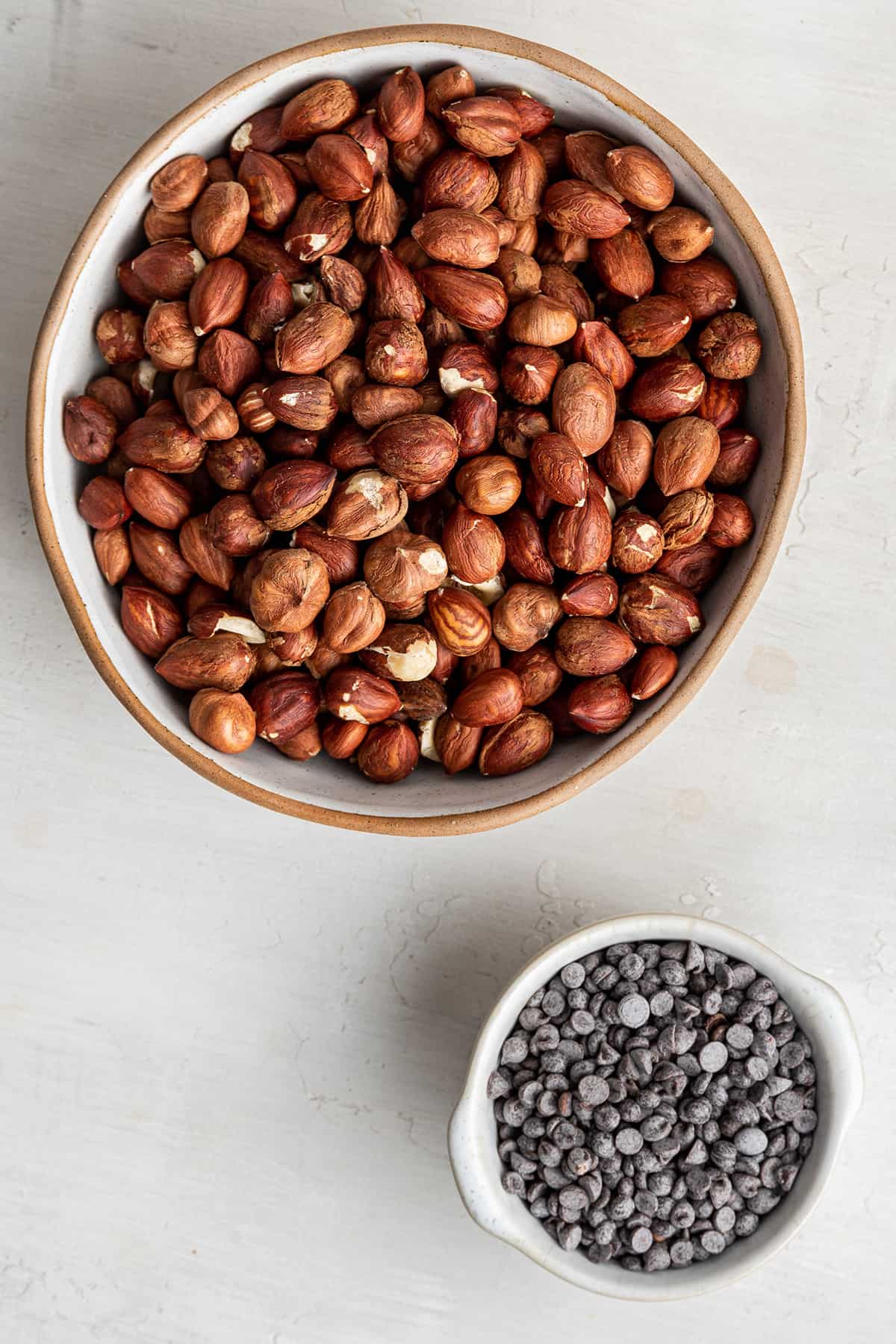 Overhead view of a large bowl full of hazelnuts and a small bowl full of chocolate chips