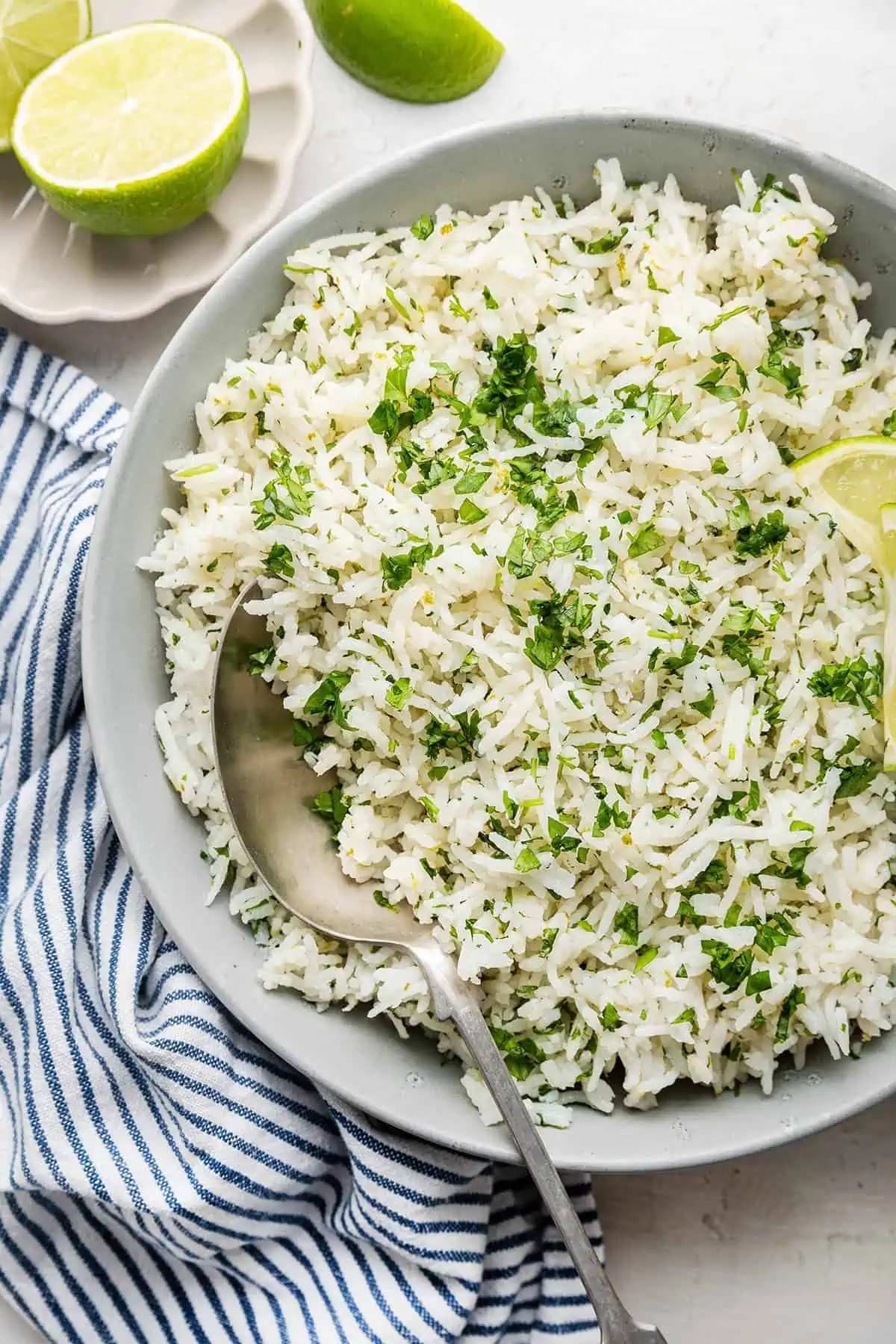 A serving tray full of cilantro lime rime with a serving spoon, next to a kitchen towel and fresh limes