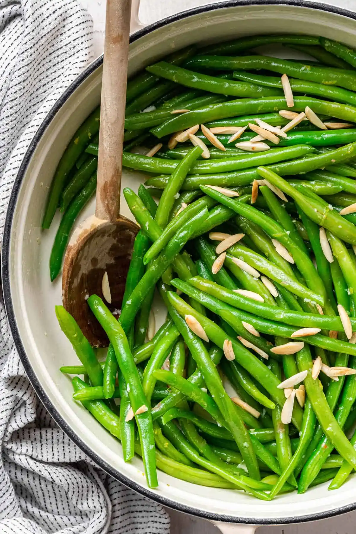 A pot of green bean almondine with a wooden spoon in it