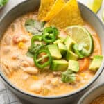 Close up of a bowl of white chicken chili garnished with tortilla chips, a lime wedge, cilantro, and chunks of avocado and chilis