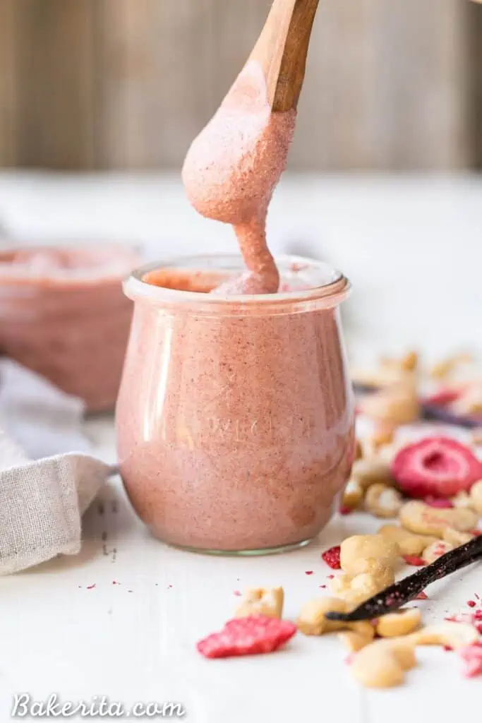 A wooden spoon stirring a jar of strawberry cashew butter.