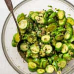 A glass bowl full of cucumber salad, with a serving spoon in it