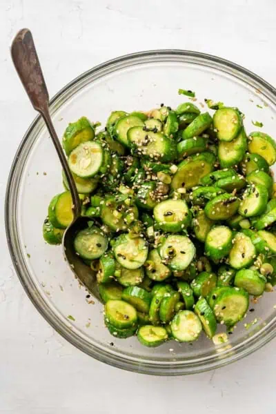 A glass bowl full of cucumber salad, with a serving spoon in it