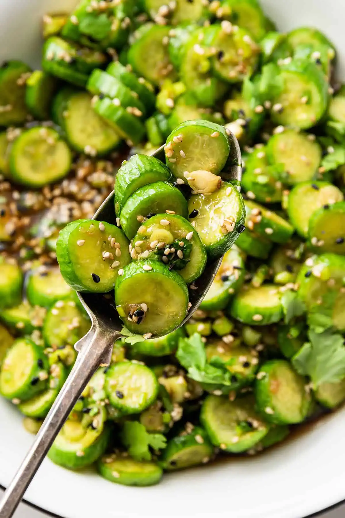 Close up of a spoonful of cucumber salad, with a bowl full of cucumber salad behind it.
