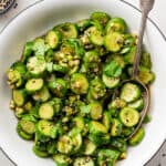 A serving bowl of cucumber salad with a serving spoon in it.