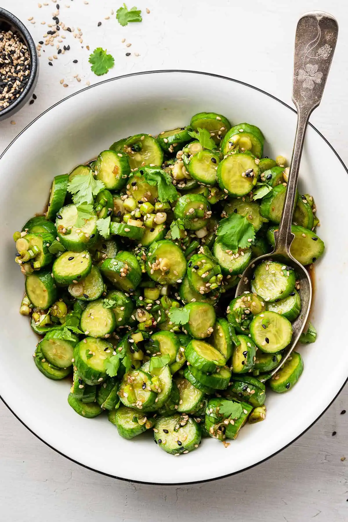 A serving bowl of cucumber salad with a serving spoon in it.