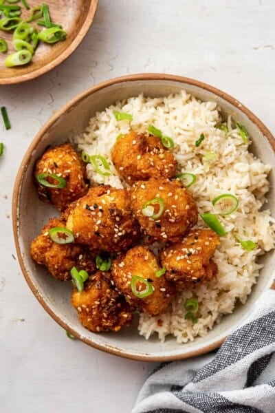 Overhead view of a bowl of rice and bang bang cauliflower topped with sesame seeds and scallions.