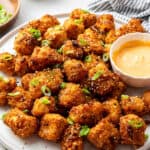 A serving tray of bang bang cauliflower with a bowl of sauce, topped with scallions.