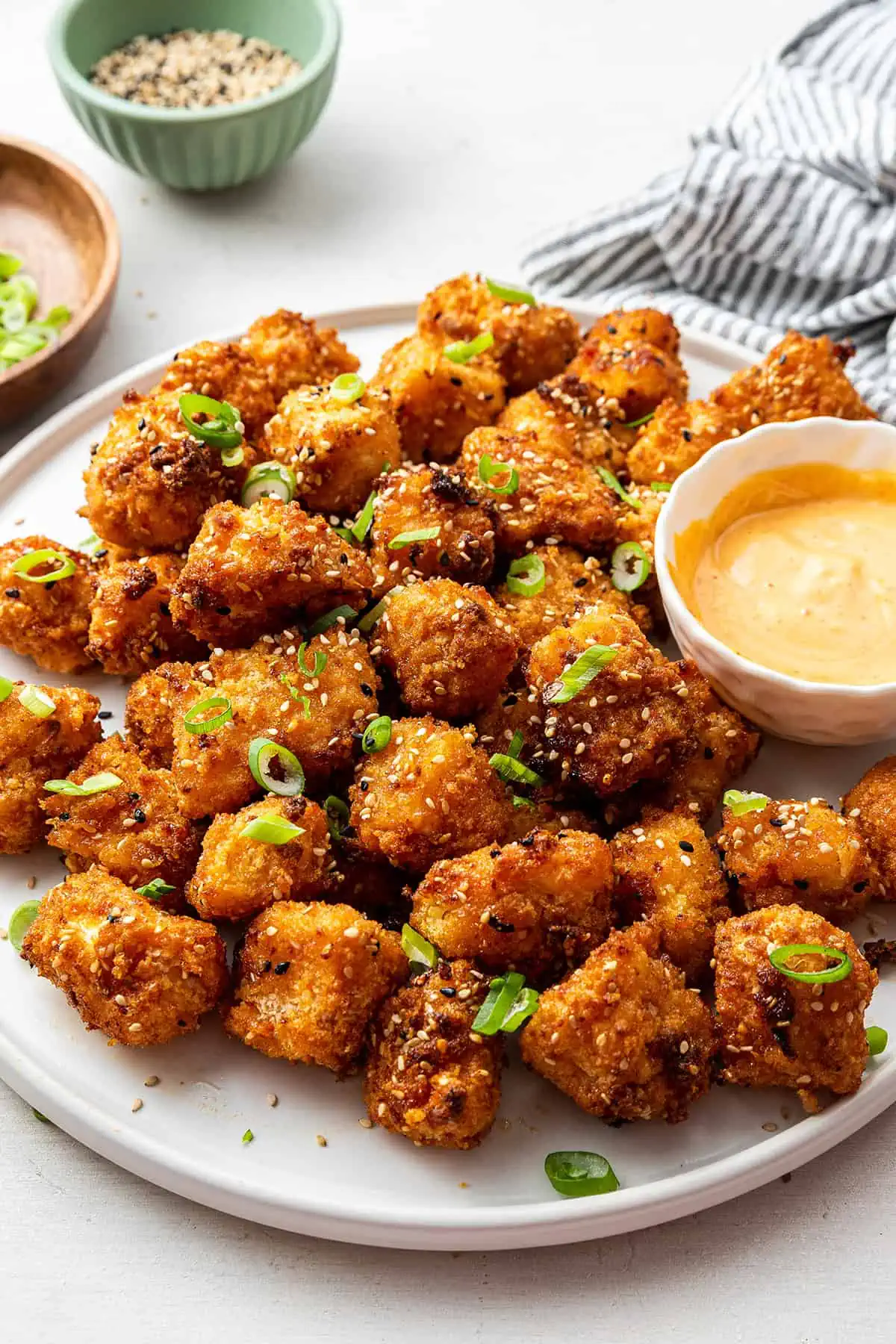 A serving tray of bang bang cauliflower with a bowl of sauce, topped with scallions.