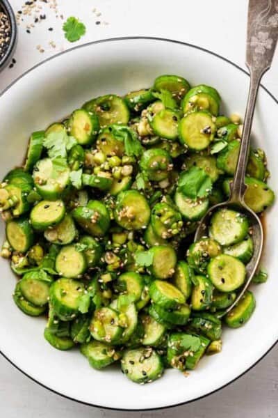 A serving bowl of cucumber salad with a serving spoon in it.