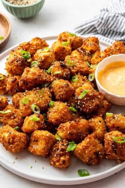 A serving tray of bang bang cauliflower with a bowl of sauce, topped with scallions.