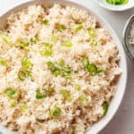 Overhead view of a serving bowl full of coconut rice topped with scallions, and a bowl of scallions.