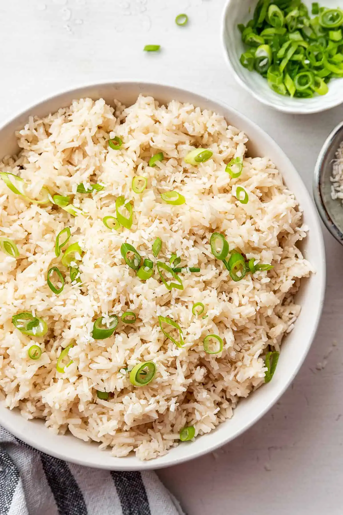 Overhead view of a serving bowl full of coconut rice topped with scallions, and a bowl of scallions.