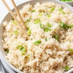 A large tray of coconut rice topped with scallions, with chopstics in it, and a bowl of scallions in the background.