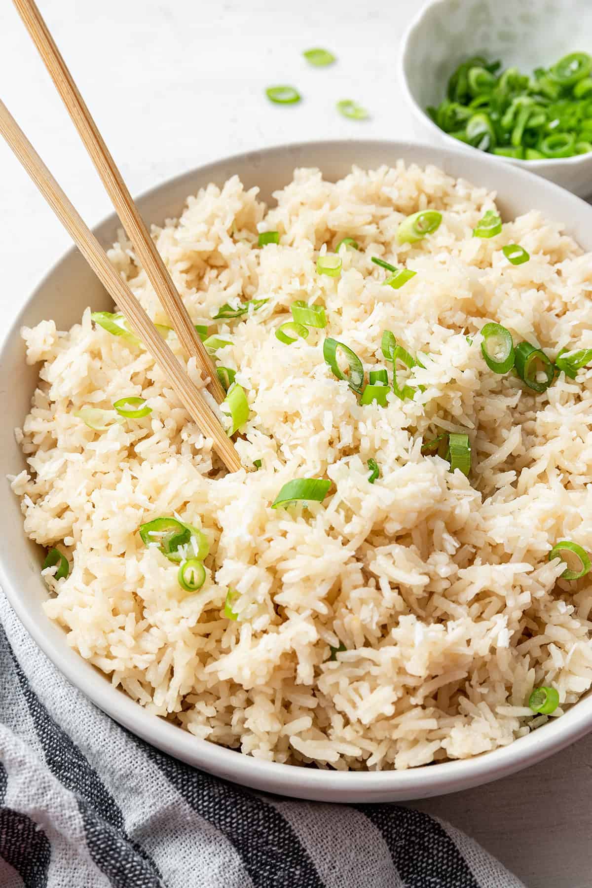 A large tray of coconut rice topped with scallions, with chopstics in it, and a bowl of scallions in the background.