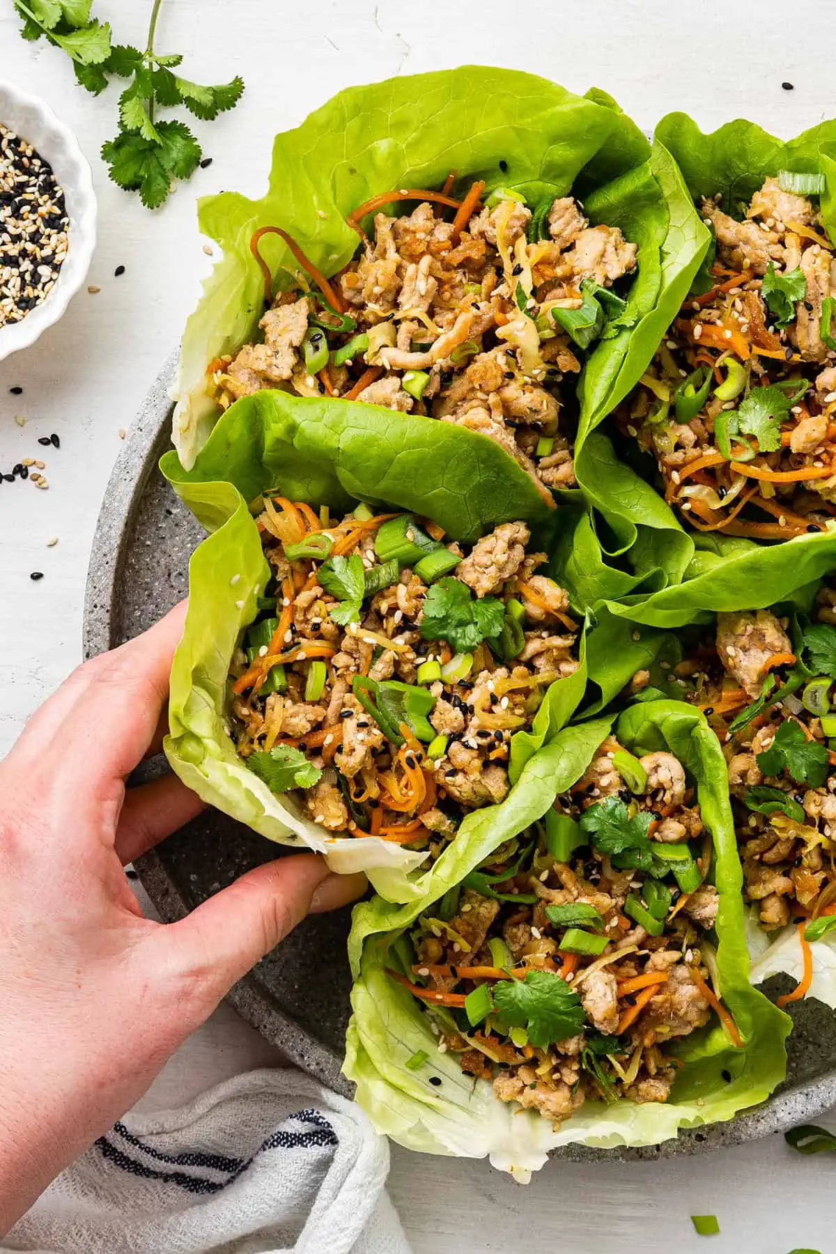 A hand grabbing for a chicken lettuce wrap on a plate with five wraps