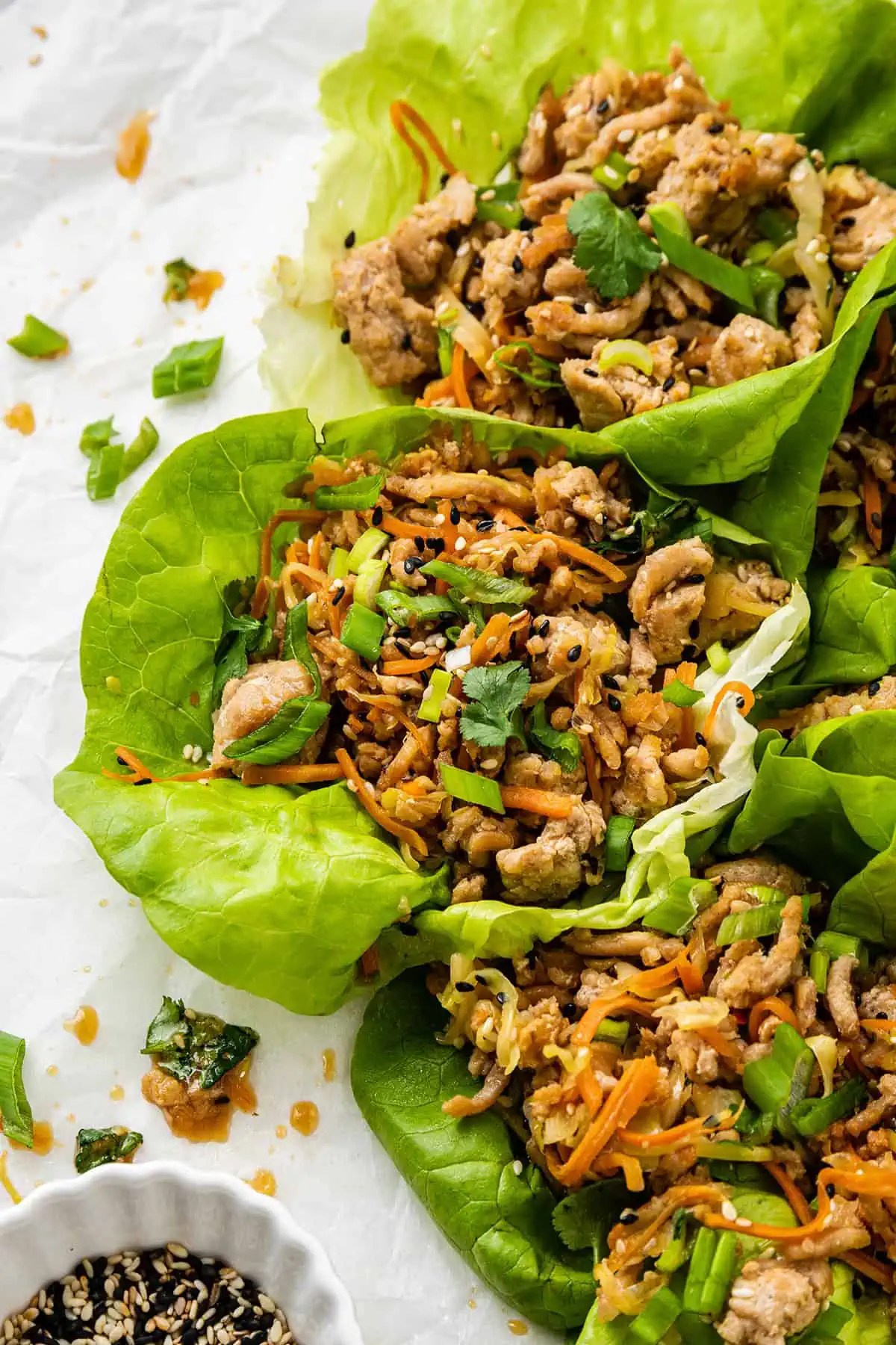 A tray of chicken lettuce wraps surrounded by sliced scallions