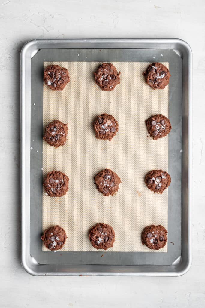These dairy-free espresso cookies are chewy, packed with chocolate and espresso flavor, and topped with the perfect touch of finishing salt. Even better, it only takes about 20 minutes to make! A baking sheet with a silpat on it, with 12 uncooked espresso cookies on it.