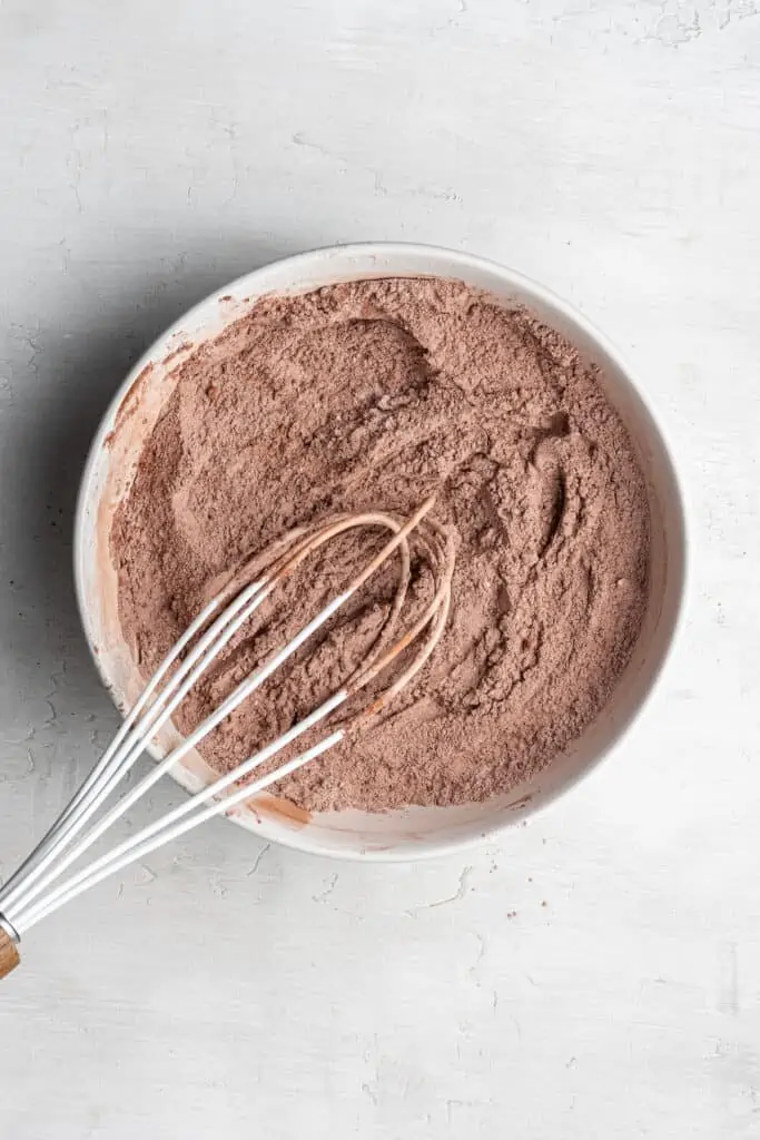 A mixing bowl with all of the dry ingredients mixed together, with a whisk in the bowl.