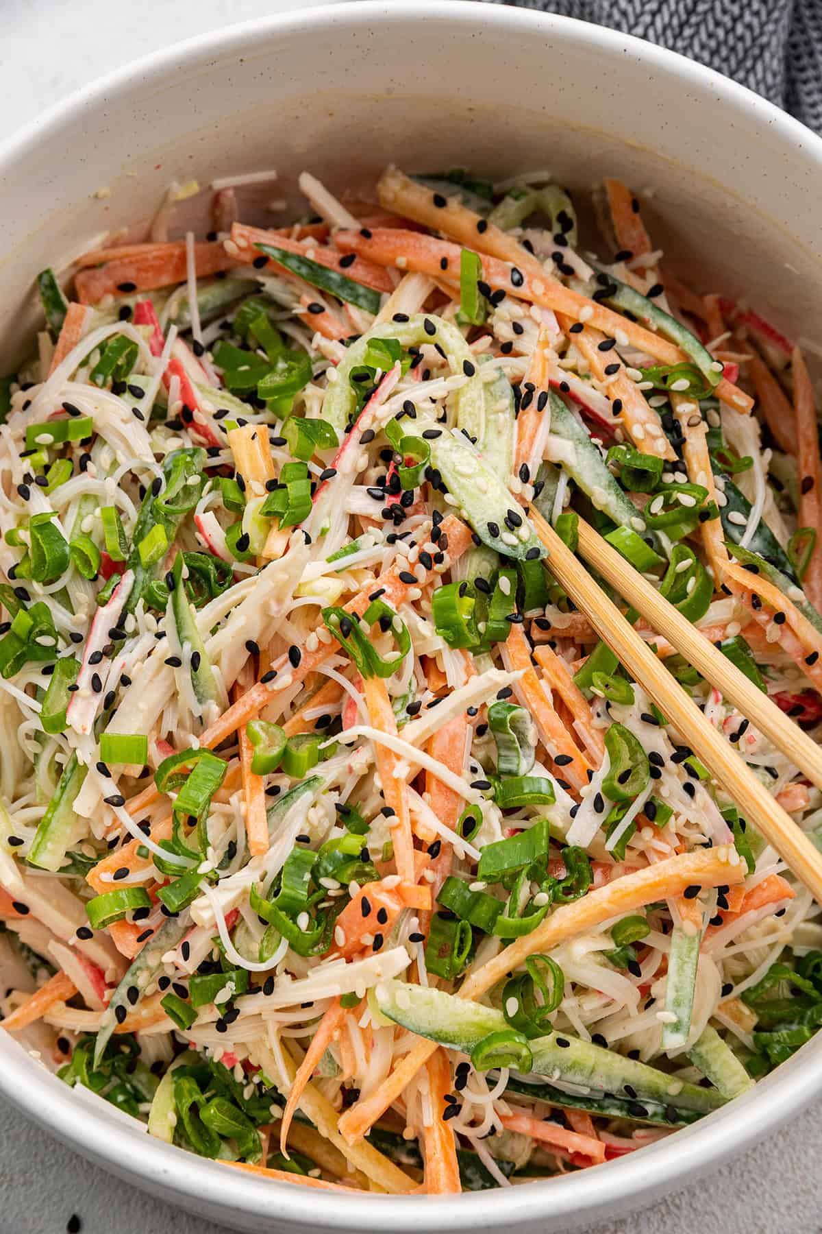 Close up overhead view of a kani salad topped with scallions and sesame seeds, with chopsticks in it