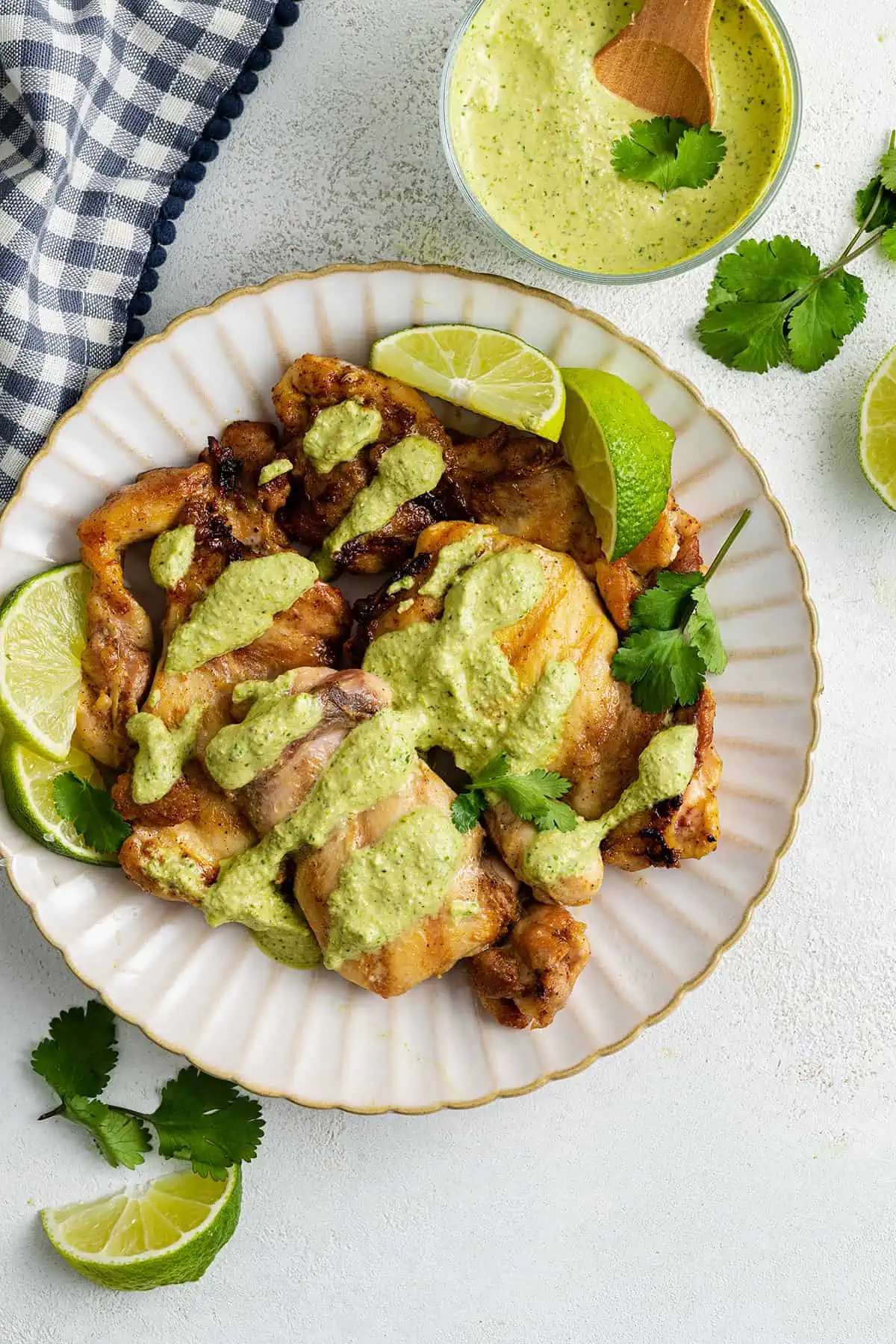 A plate with grilled chicken covered in cilantro lime sauce, topped with cilantro leaves and lime slices