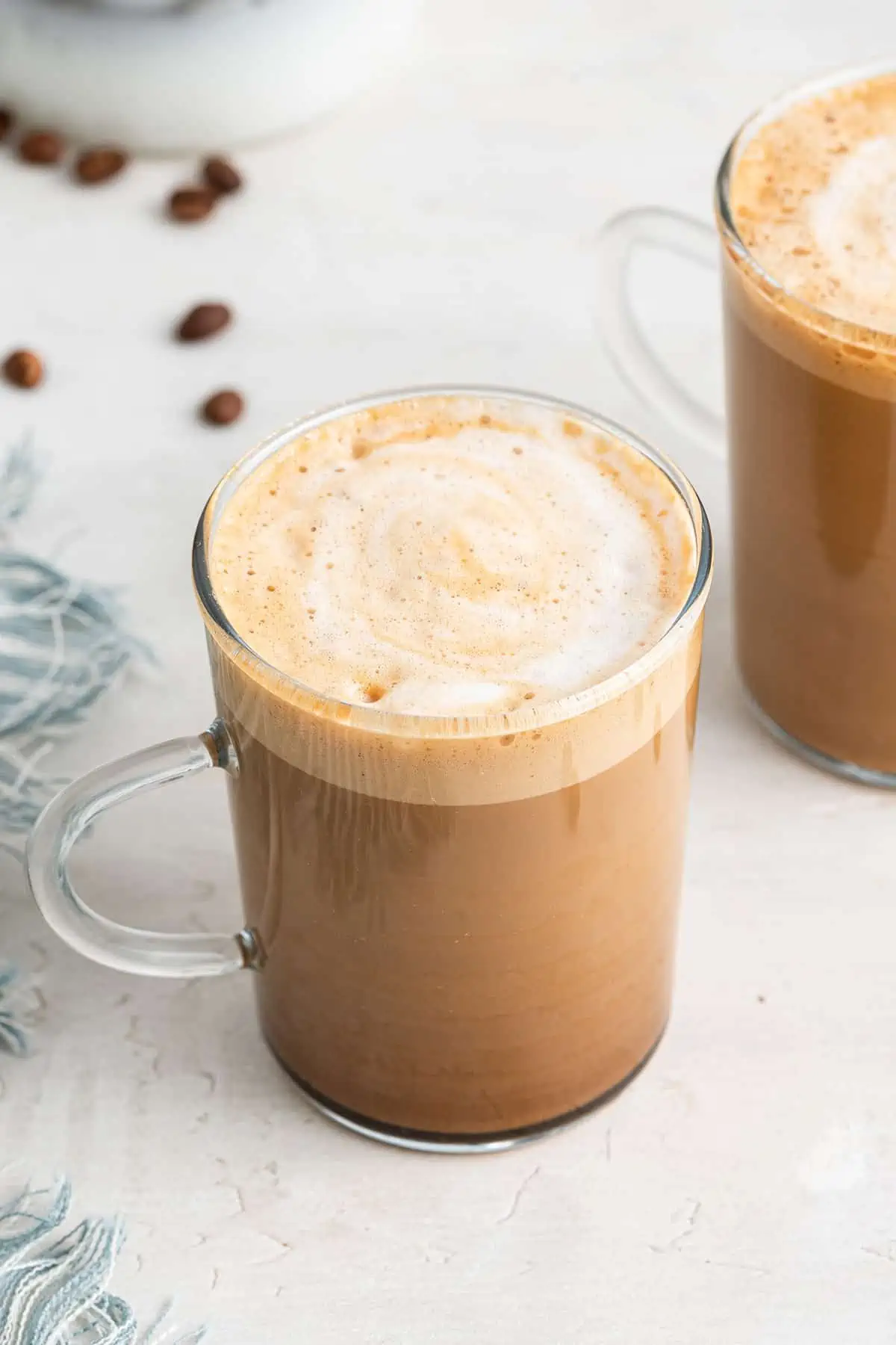 A cortadito in a glass, next to another cortadito, with coffee beans behind it