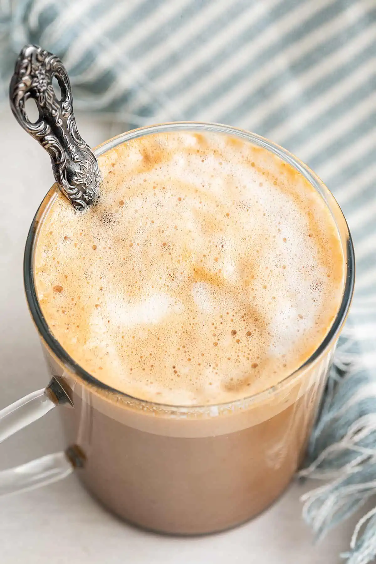 Overhead view of a cortadito in a glass, with a spoon in it, next to a kitchen towel