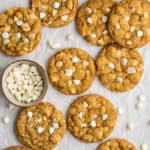 Overhead view of a bunch of white chocolate chip and macadamia nut cookies, with a jar of milk and a bowl of white chocolate chips