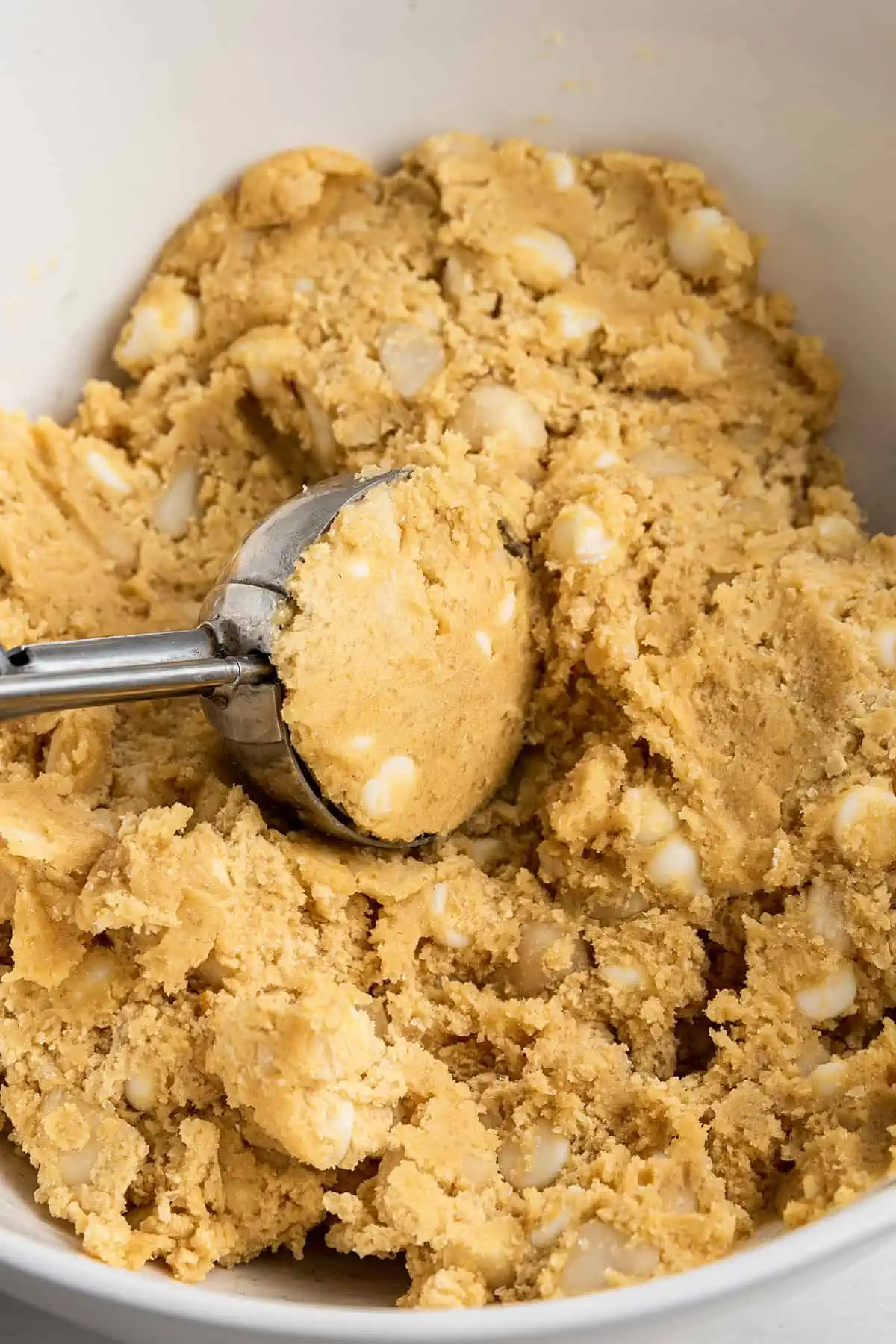 A cookie dough scooper scooping out a ball of cookie dough from a bowl
