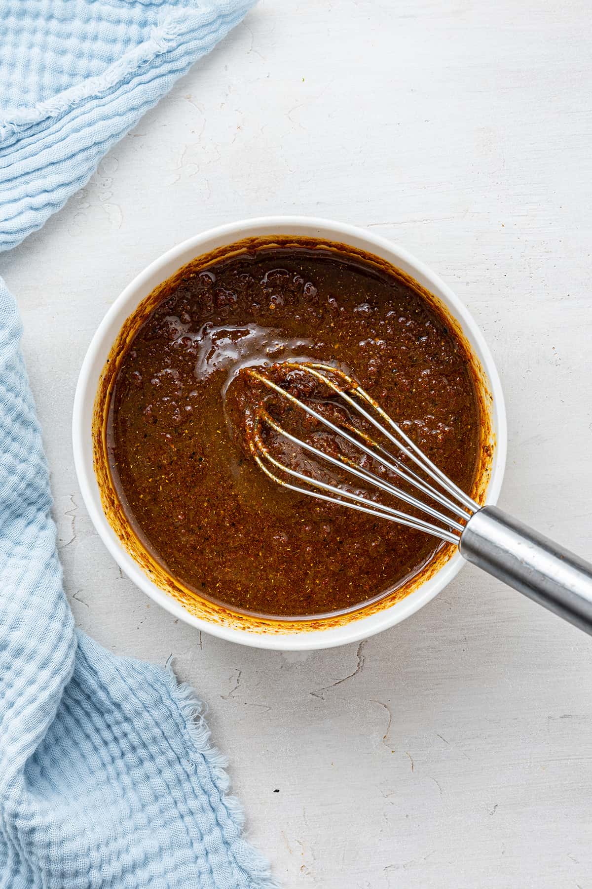 This Moroccan chicken recipe has juicy and tender thigh meat, a sweet and tangy sauce, and is topped with olives and slivered almonds. A mixing bowl with a brown sauce, with a whisk in it