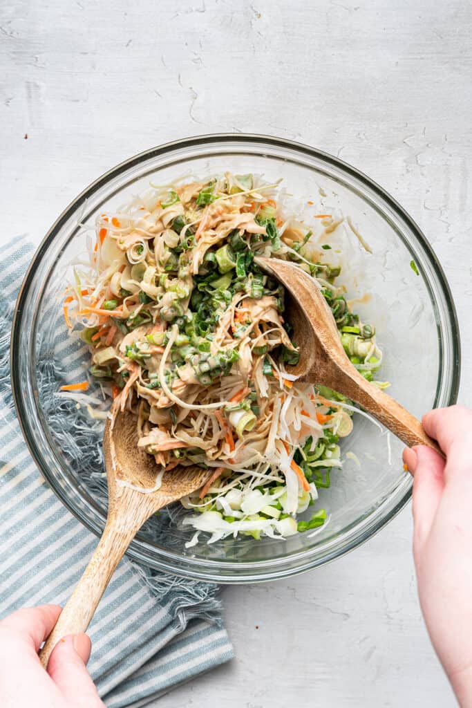 Slaw in a mixing bowl being tossed with two salad forks